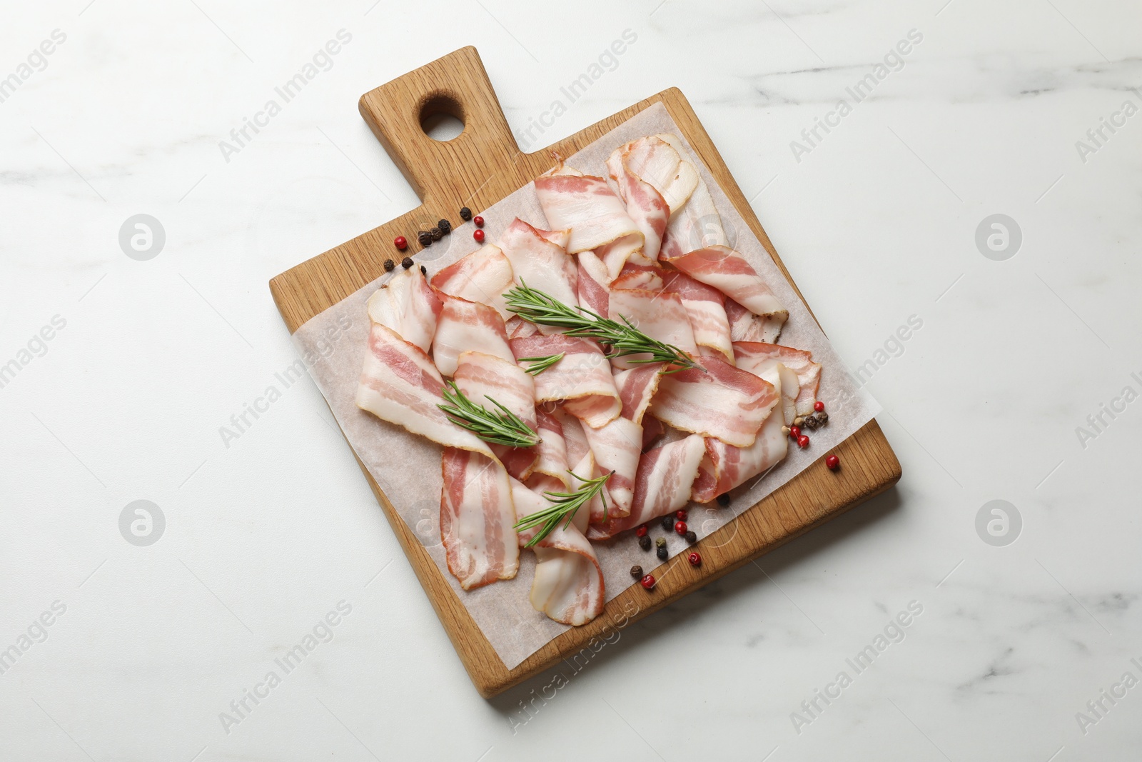 Photo of Slices of raw bacon and spices on white marble table, top view