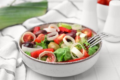 Bowl of tasty salad with leek and olives on white tiled table, closeup