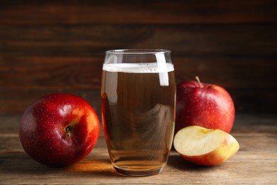 Glass of delicious cider and ripe red apples on wooden table