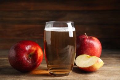 Photo of Glass of delicious cider and ripe red apples on wooden table