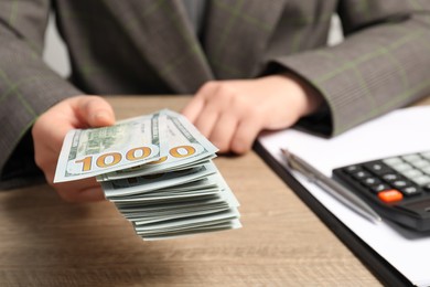 Photo of Money exchange. Woman holding dollar banknotes at wooden table, closeup