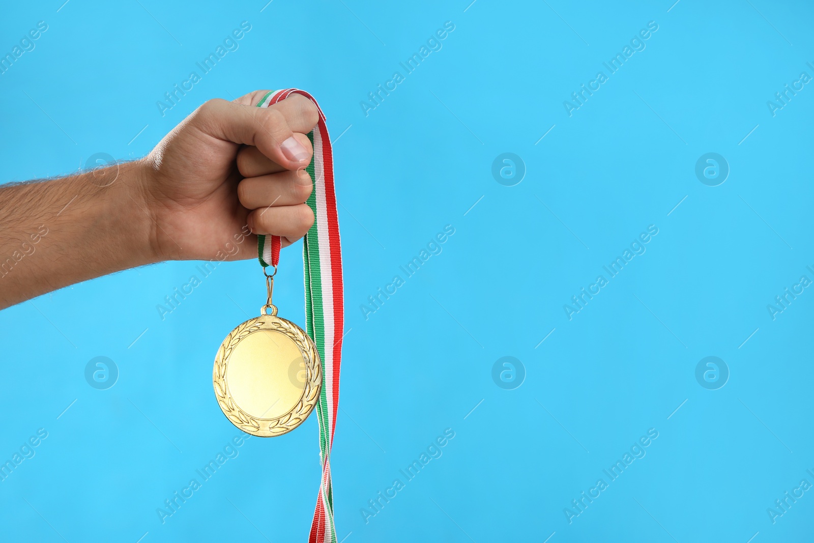 Photo of Man holding golden medal on light blue background, closeup. Space for design