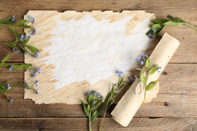 Beautiful forget-me-not flowers and sheets of old parchment paper on wooden table, top view