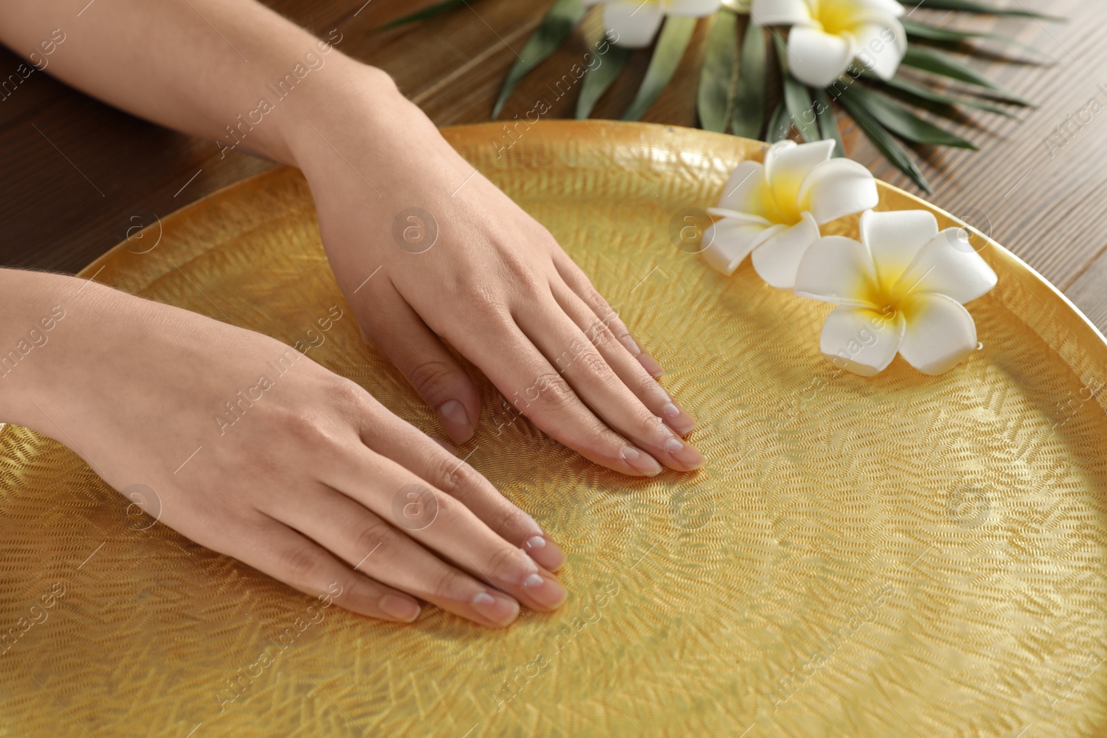 Photo of Woman soaking her hands in bowl with water and flowers on table, closeup. Spa treatment