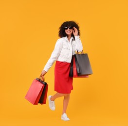 Photo of Happy young woman with shopping bags and stylish sunglasses on yellow background