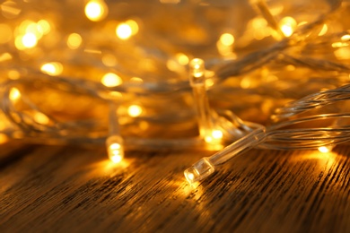 Glowing Christmas lights on wooden table, closeup view