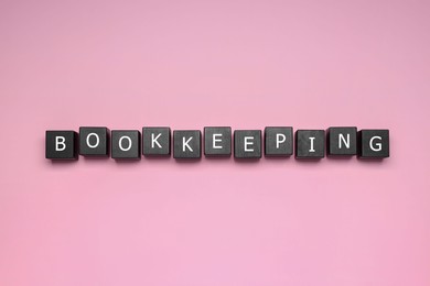 Photo of Word Bookkeeping made with black cubes on pink background, top view
