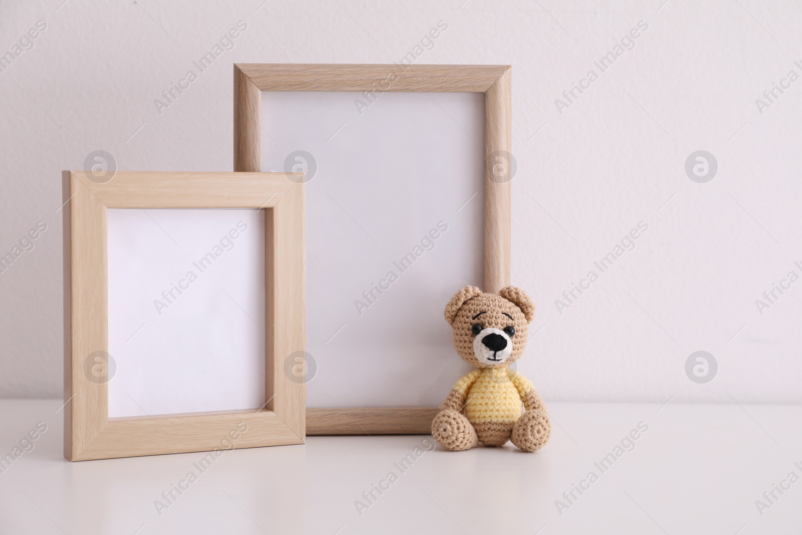 Photo of Empty photo frames and toy bear on table near white wall. Space for design