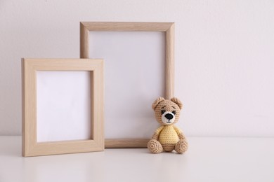 Photo of Empty photo frames and toy bear on table near white wall. Space for design