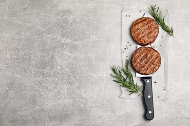 Tasty grilled hamburger patties, knife and seasonings on grey table, flat lay. Space for text