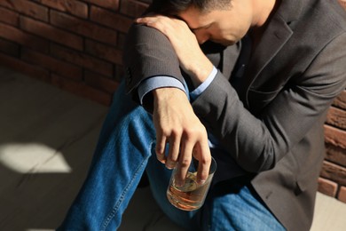 Addicted man with glass of alcoholic drink near red brick wall, closeup
