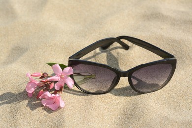 Beautiful sunglasses with flower on sandy beach