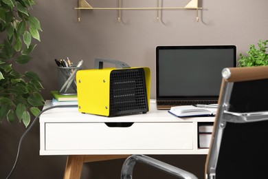 Modern electric fan heater near laptop and notebooks on white table in office