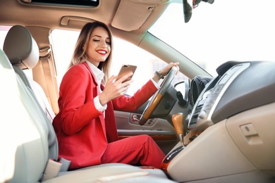 Young businesswoman with smartphone on driver's seat of car