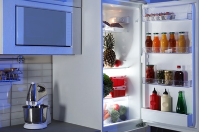 Photo of Open refrigerator full of products in stylish kitchen interior at night