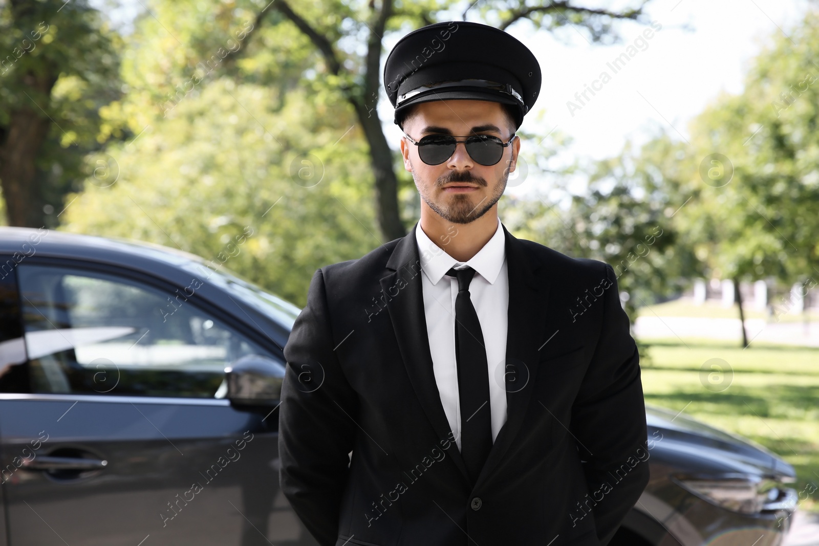 Photo of Young handsome driver standing near luxury car. Chauffeur service