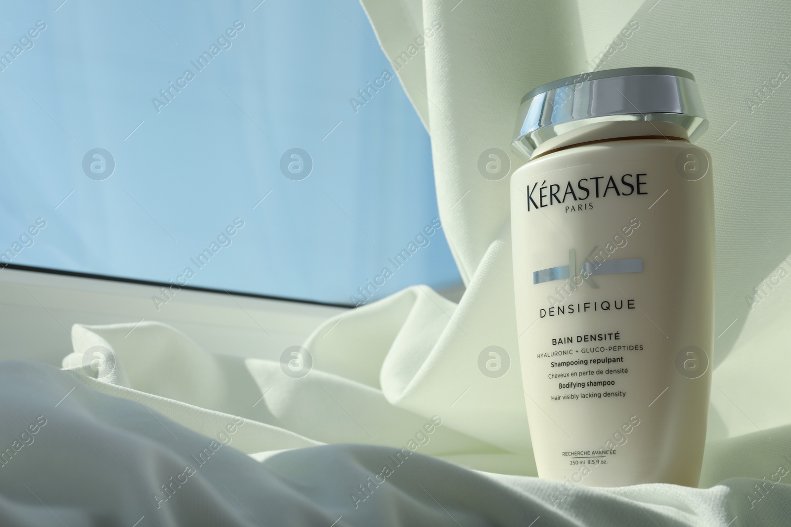 Photo of MYKOLAIV, UKRAINE - SEPTEMBER 07, 2021: Kerastase shampoo on white fabric, space for text. Hair care cosmetic product