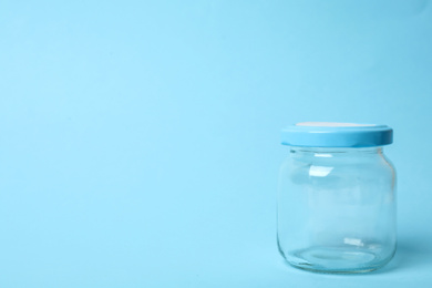 Photo of Closed empty glass jar on light blue background, space for text