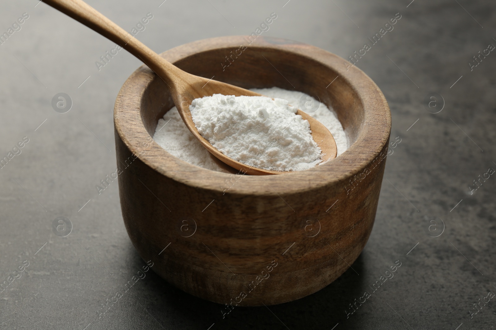 Photo of Baking powder in bowl and spoon on grey textured table