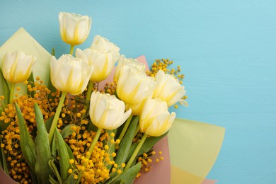 Bouquet with beautiful tulips and mimosa flowers on light blue wooden table, top view. Space for text