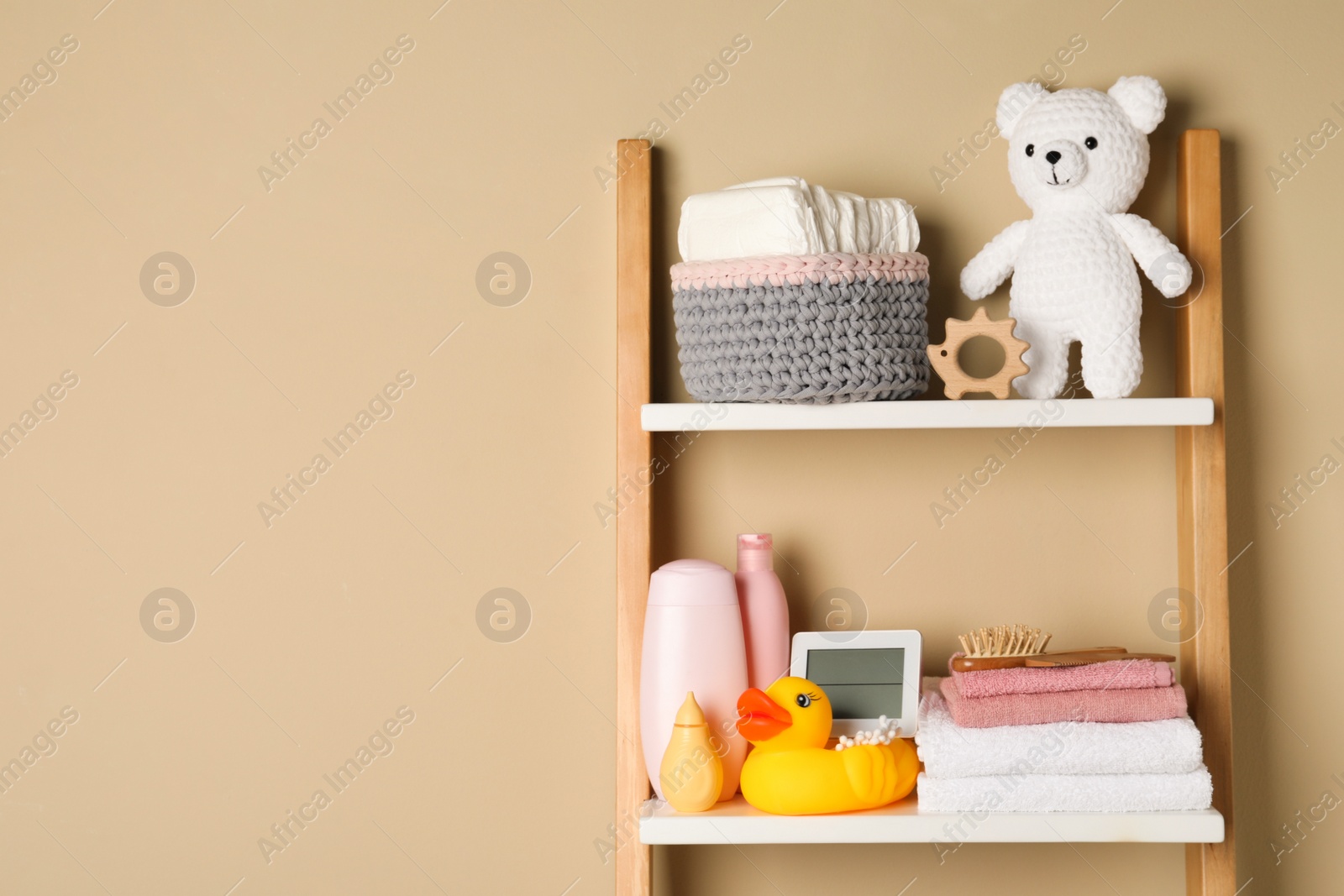 Photo of Towels, toys and baby accessories on wooden rack, space for text