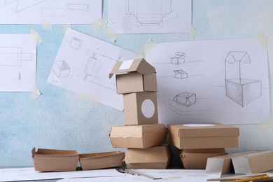 Photo of Creating packaging design. Drawings, boxes and stationery on table, closeup