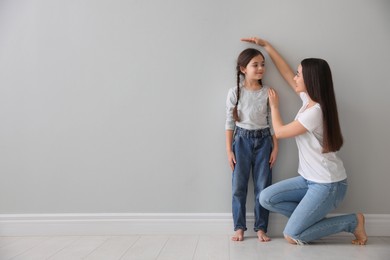 Photo of Mother measuring little girl's height near light grey wall indoors. Space for text