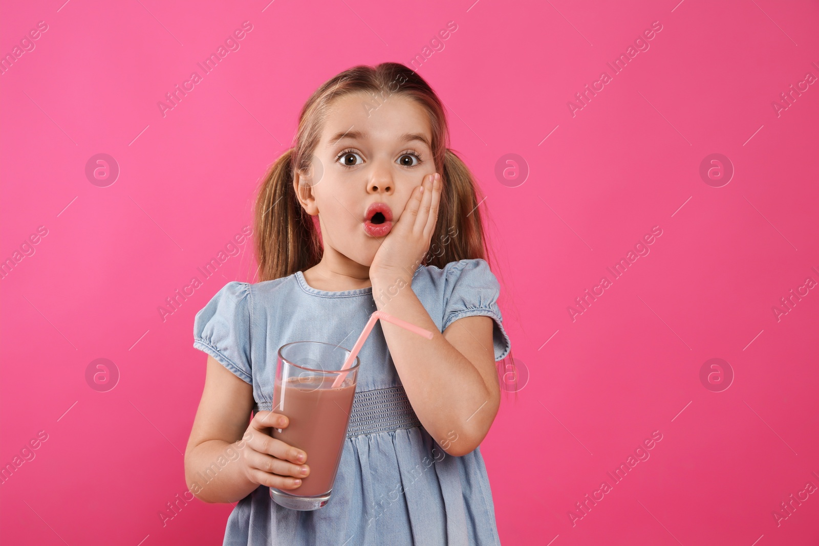 Photo of Surprised little child with glass of tasty chocolate milk on pink background, space for text
