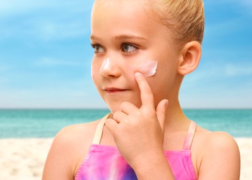 Image of Sun protection. Cute girl applying sunblock onto face on beach, closeup