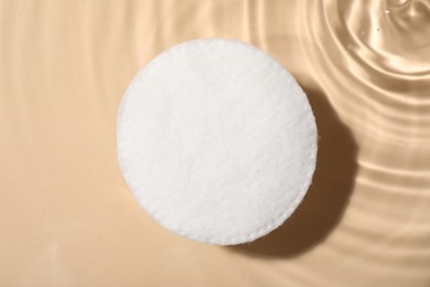 Photo of Cotton pad and micellar water on beige background, top view