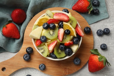 Photo of Tasty fruit salad in bowl and ingredients on gray textured table, flat lay