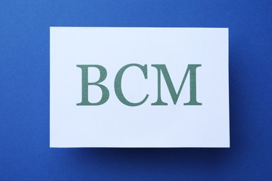 Photo of White paper with abbreviation BCM (Business Continuity Management) on blue background, top view