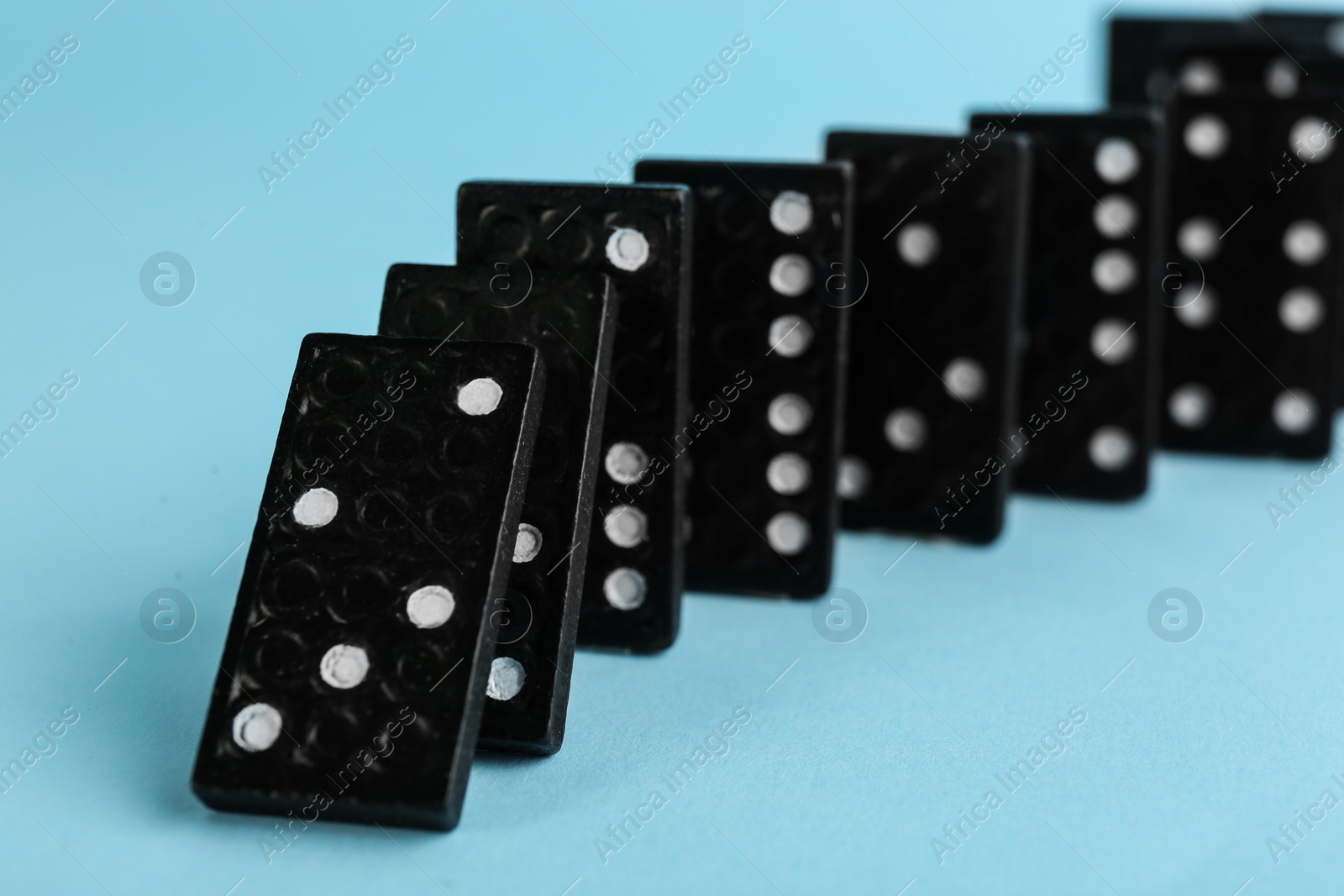 Photo of Black domino tiles falling on light blue background, closeup