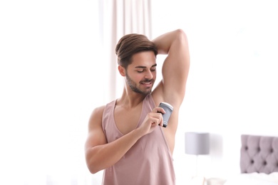 Photo of Handsome young man applying deodorant in bedroom