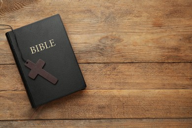 Photo of Christian cross and Bible on wooden table, top view. Space for text