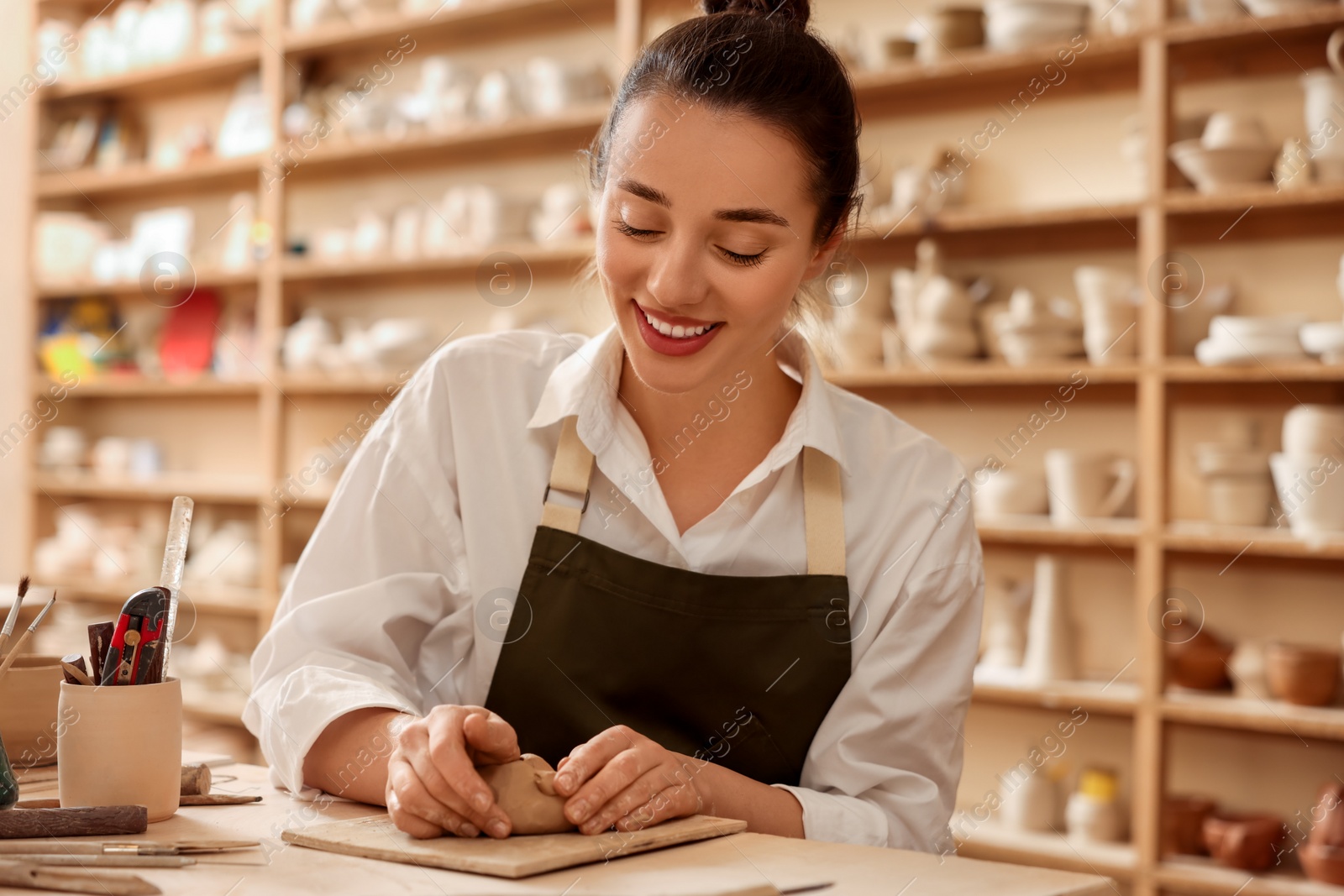 Photo of Smiling woman crafting with clay at table in workshop