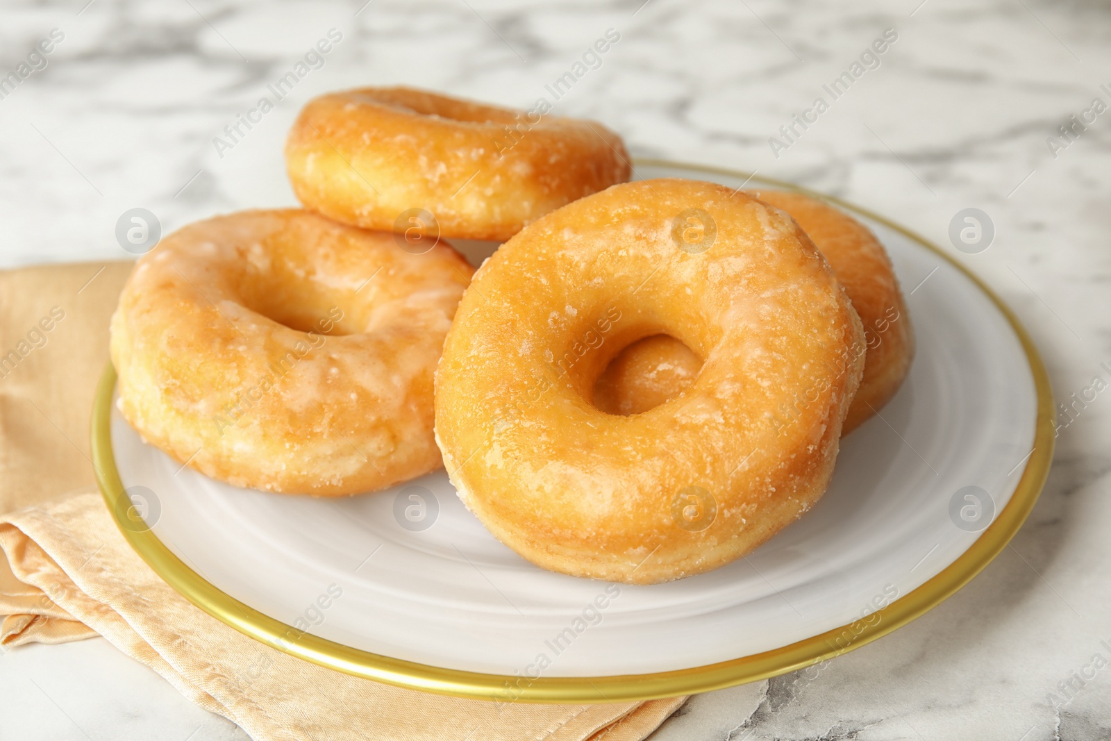 Photo of Delicious glazed donuts on marble table, closeup