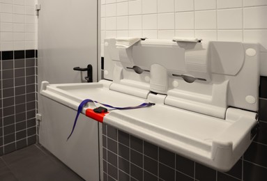 Photo of Modern baby changing table on tiled wall in public toilet