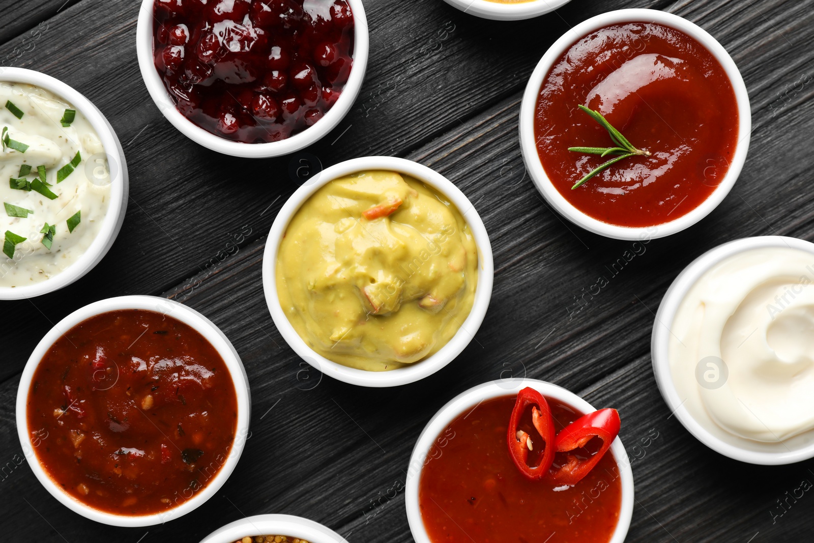 Photo of Different tasty sauces in bowls on black wooden table, flat lay