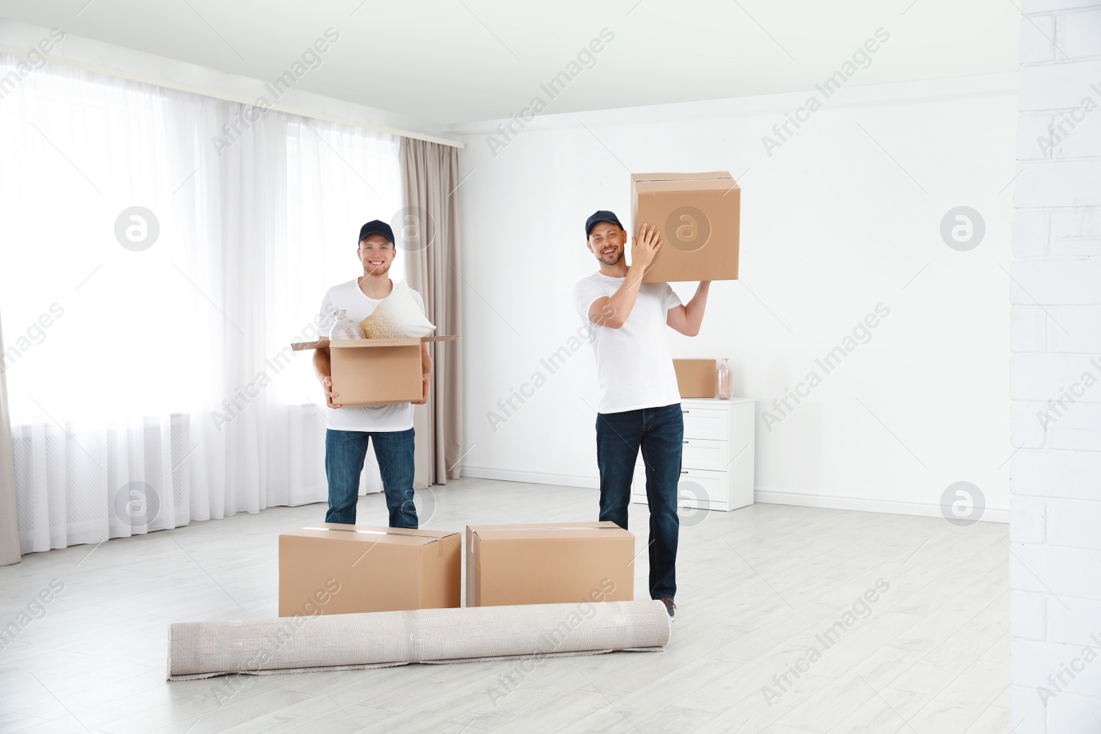 Photo of Moving service employees with cardboard boxes in room