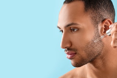 Photo of Handsome man applying cosmetic serum onto face on light blue background, closeup. Space for text