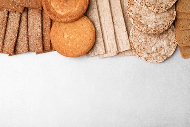 Rye crispbreads, rice cakes and rusks on white table, flat lay. Space for text