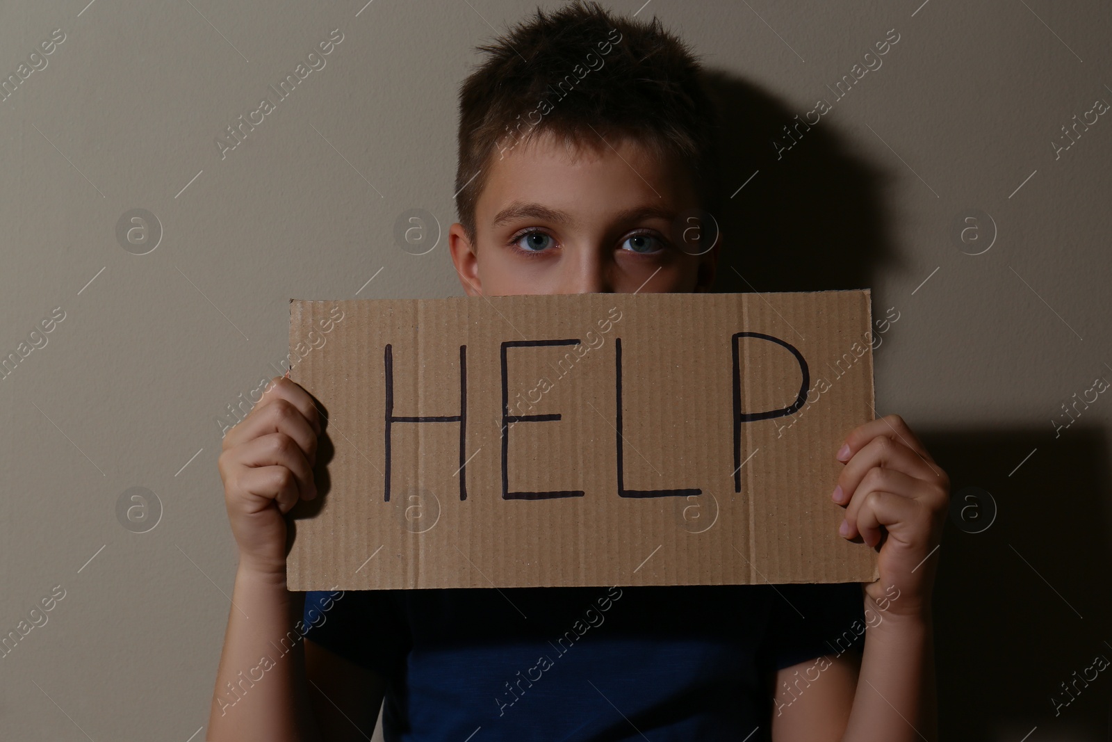 Photo of Abused little boy with sign HELP near beige wall. Domestic violence concept