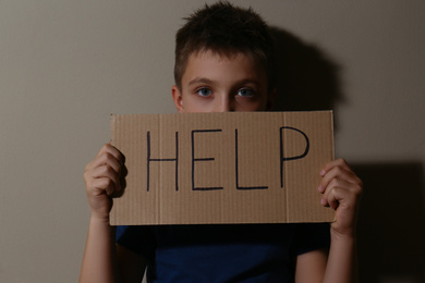 Abused little boy with sign HELP near beige wall. Domestic violence concept