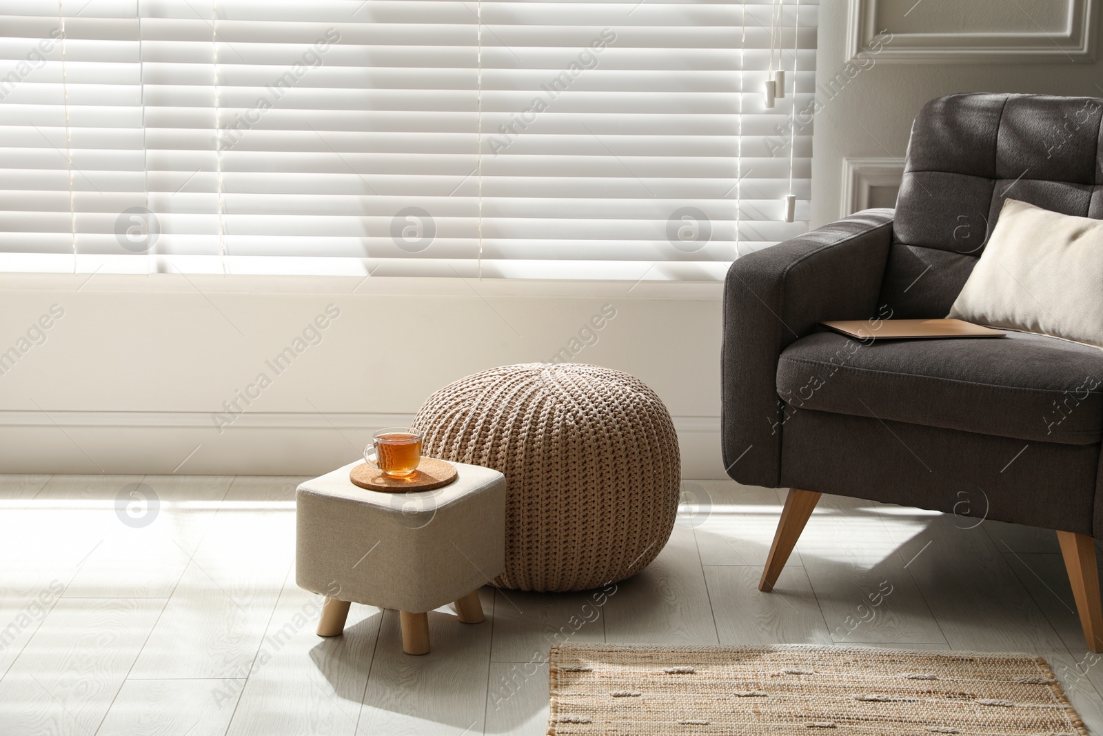 Photo of Tray with cup of tea on stylish ottoman and comfortable pouf in room