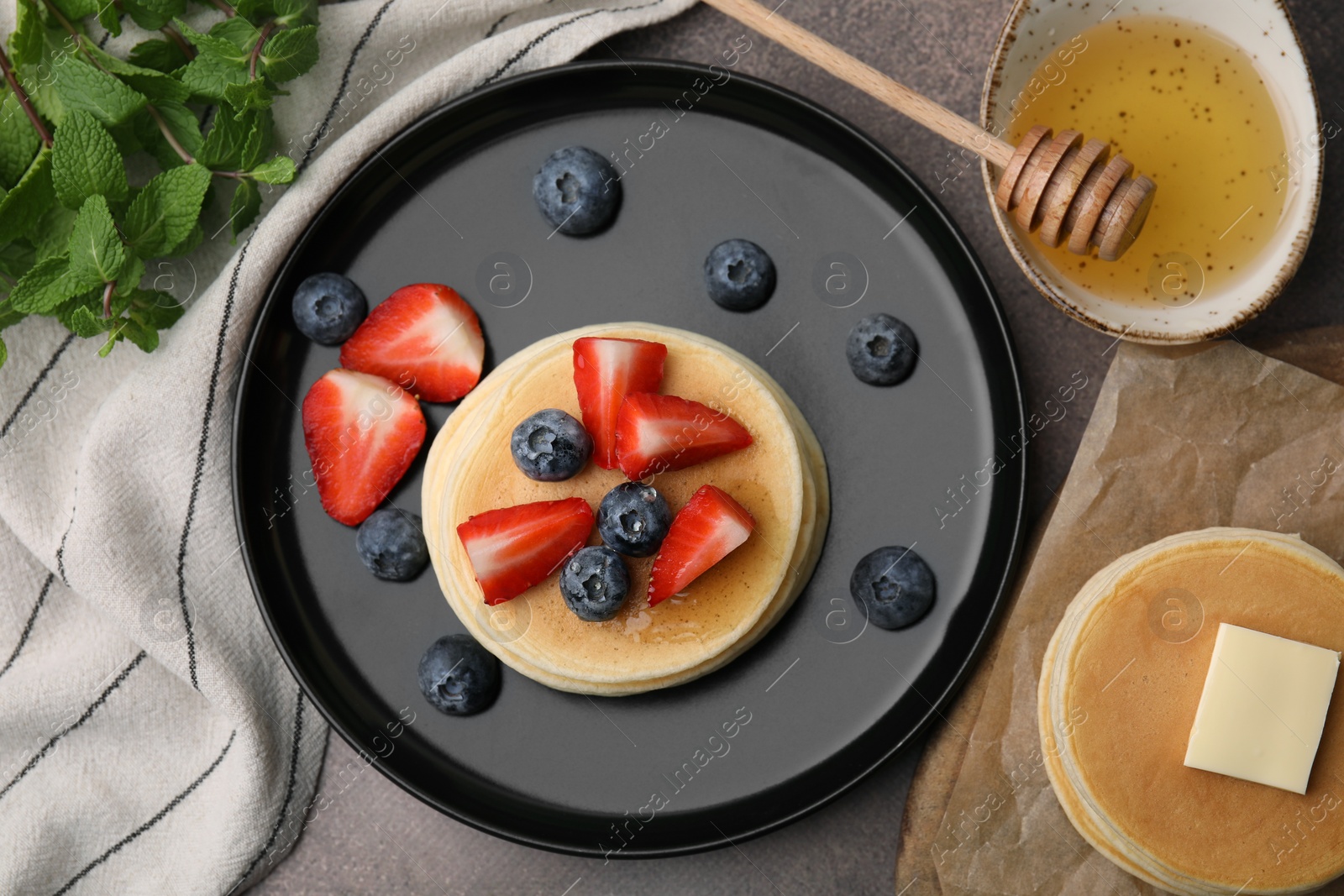 Photo of Delicious pancakes with strawberries and blueberries served on brown table, flat lay