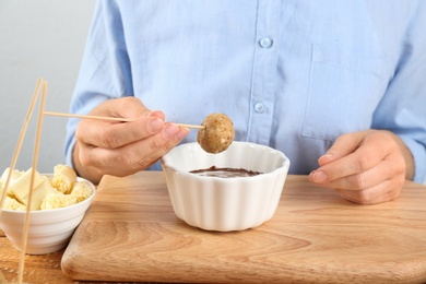 Young woman with cake pop and chocolate frosting on wooden board, closeup