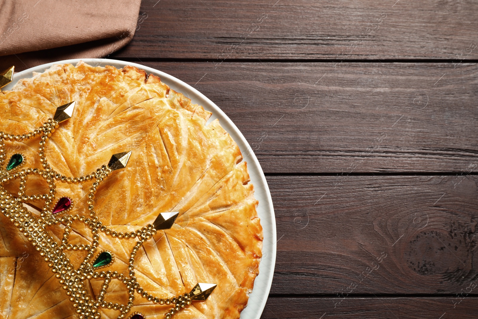 Photo of Traditional galette des rois with decorative crown on wooden table, top view. Space for text