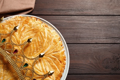 Photo of Traditional galette des rois with decorative crown on wooden table, top view. Space for text