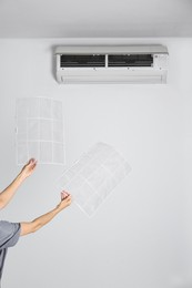 Photo of Woman holding filters under air conditioner indoors, closeup
